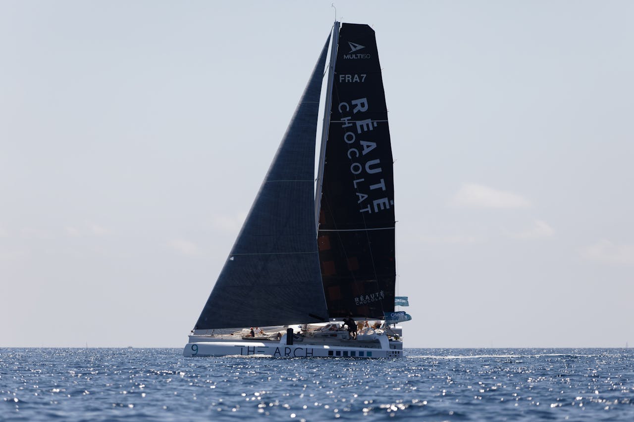 A sleek sailing yacht glides over calm ocean waves under a clear blue sky, capturing serene maritime beauty.